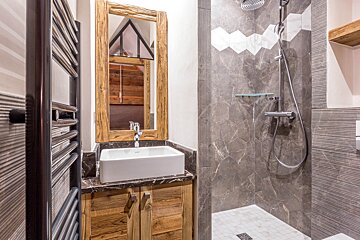 Modern rustic bathroom featuring a wooden vanity with a vessel sink and a gray tiled walk-in shower.