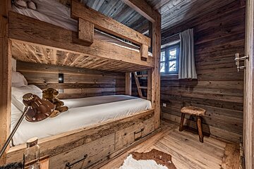 A cozy, rustic wooden bedroom featuring sturdy bunk beds, wood-paneled walls, a window, and a teddy bear, evoking a warm cabin ambiance.