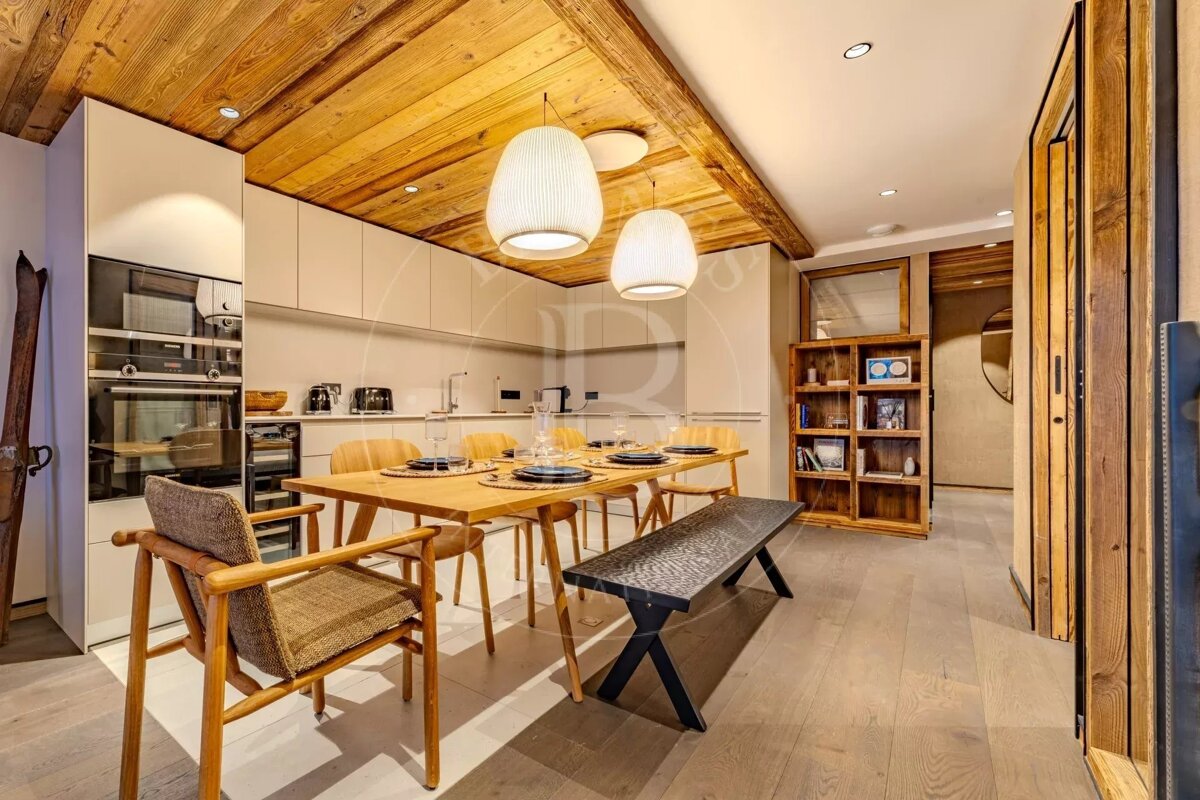 A modern alpine kitchen and dining area with a wooden ceiling, a dining table set, and two white pendant lights.