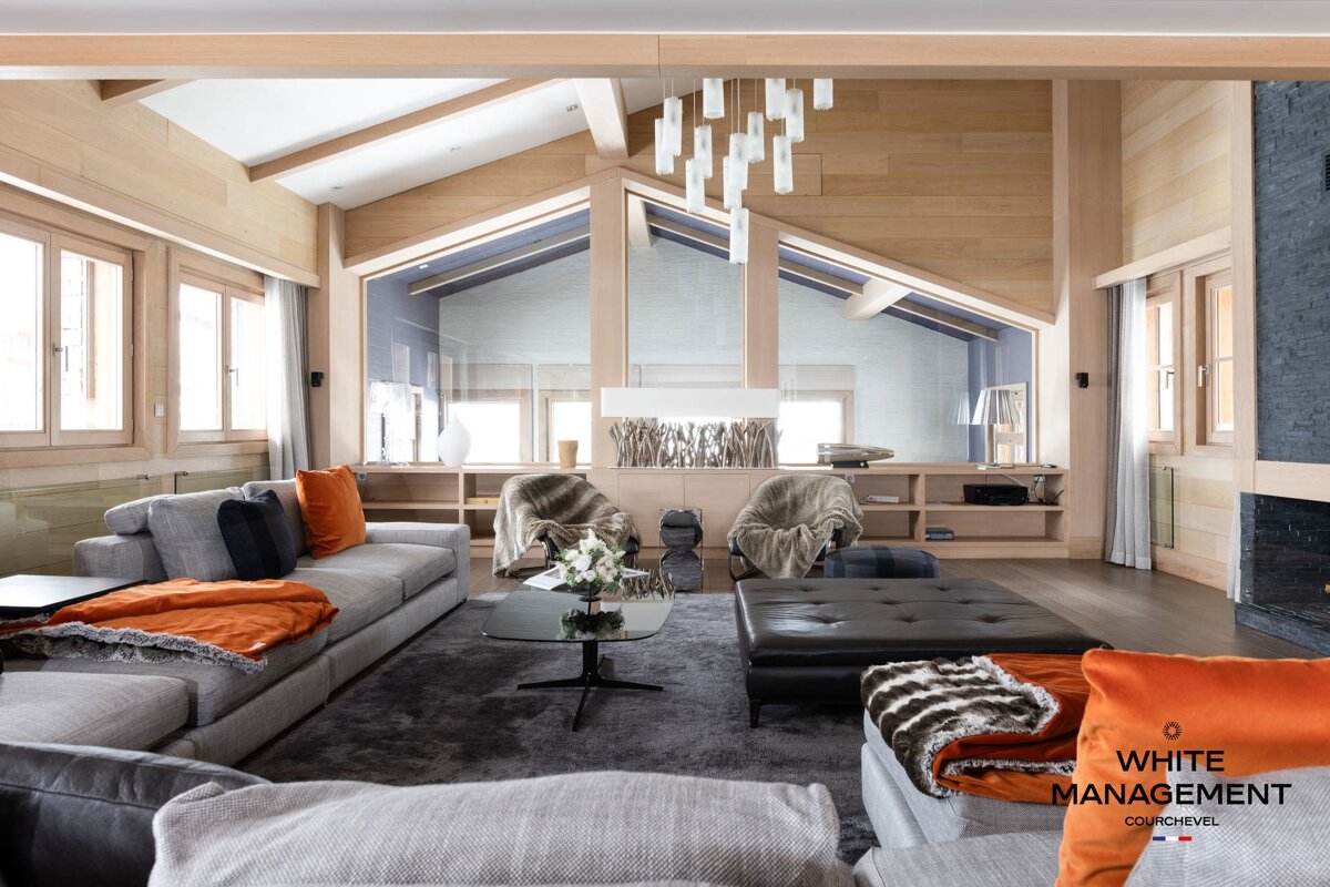 A luxurious modern chalet living room featuring wood paneling, gray sofas, and orange accents.