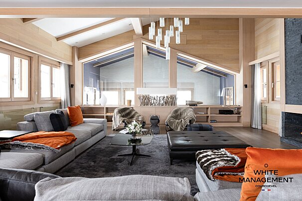 A luxurious modern chalet living room featuring wood paneling, gray sofas, and orange accents.