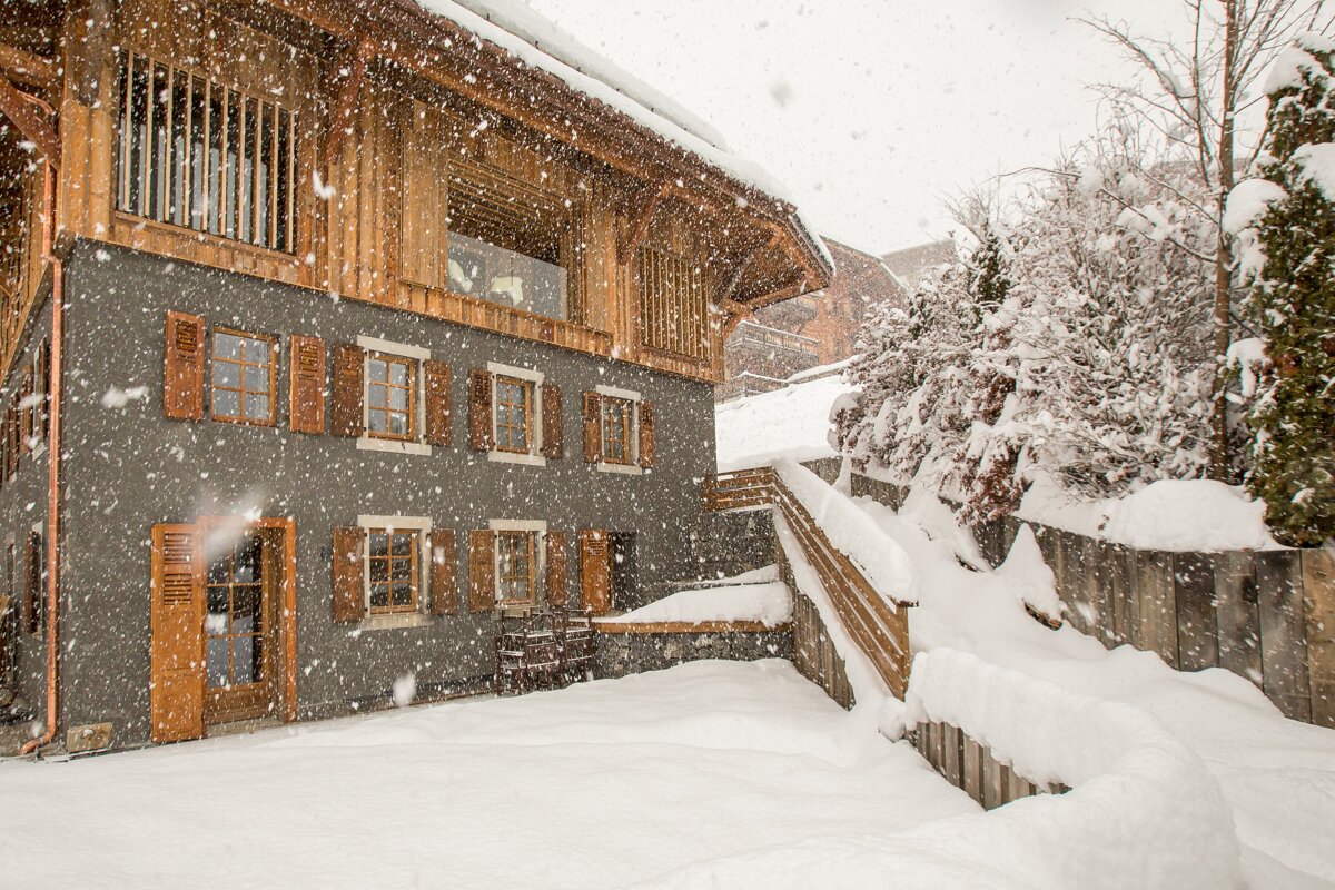 Snow is falling on a house with wooden shutters