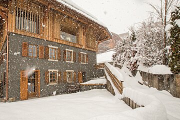 Snow is falling on a house with wooden shutters