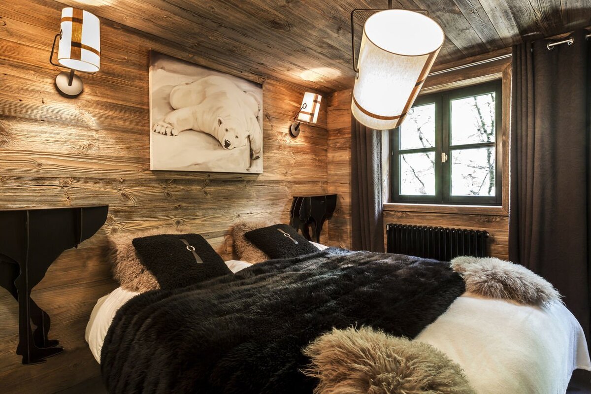 Cozy, wood-paneled bedroom with a large bed, faux fur throws, and a polar bear art piece. A window overlooks a winter scene.
