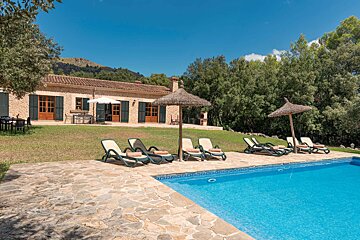 A swimming pool with chairs and umbrellas in front of a house