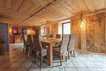 Cozy, rustic dining room featuring warm wood paneling, a large wooden table with wicker chairs, and unique rope chandeliers.
