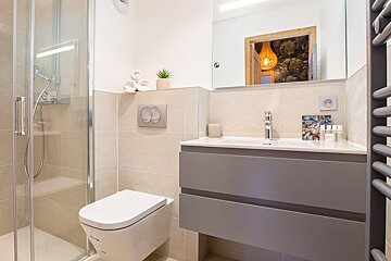 A clean, modern bathroom featuring a glass shower, a white toilet, a grey floating vanity, and beige wall tiling.