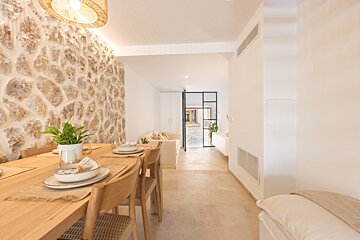 Bright, modern dining room featuring a long wooden table, stone accent wall, and an open layout leading to a minimalist living space.