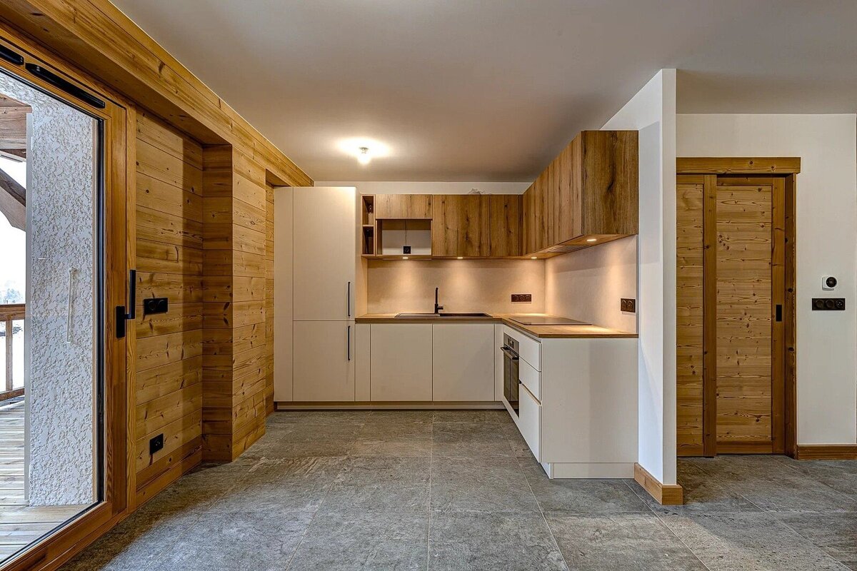 Modern kitchen featuring white and wooden cabinets, rustic wood paneling on the walls, and a grey tiled floor.