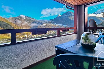 Balcony overlooking a snow-dusted mountain valley and village under a clear blue sky. An outdoor table with a terrarium is visible.