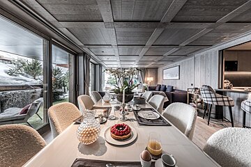 Chic chalet dining room with a breakfast-laden table, plush seating, and large windows overlooking a snowy outdoor scene.