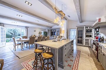 Elegant open-concept kitchen and dining space with exposed beams, a central island, and French doors leading to a lush garden.