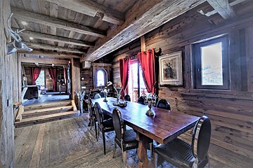 Inviting chalet dining room with rich wooden walls, floors, and ceiling beams, accented by vibrant red curtains and elegant table decor.