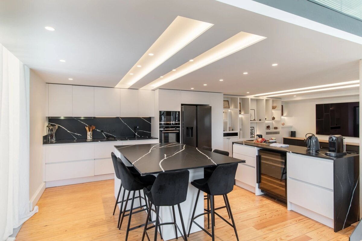 Modern kitchen featuring white cabinets, a black marble island with bar stools, wooden floors, and sleek recessed ceiling lighting.