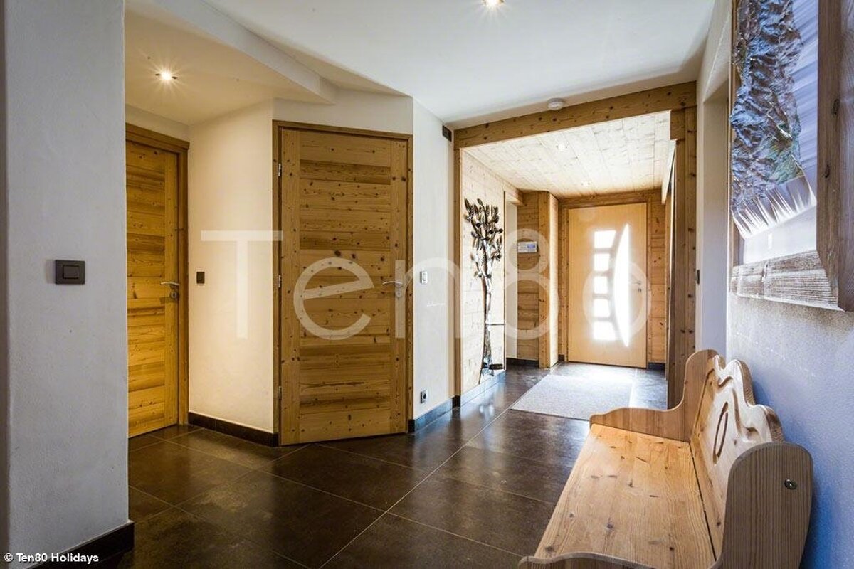 Rustic modern entryway featuring dark tile floors, pine wood doors, a matching bench, and a bright, sunlit entrance.