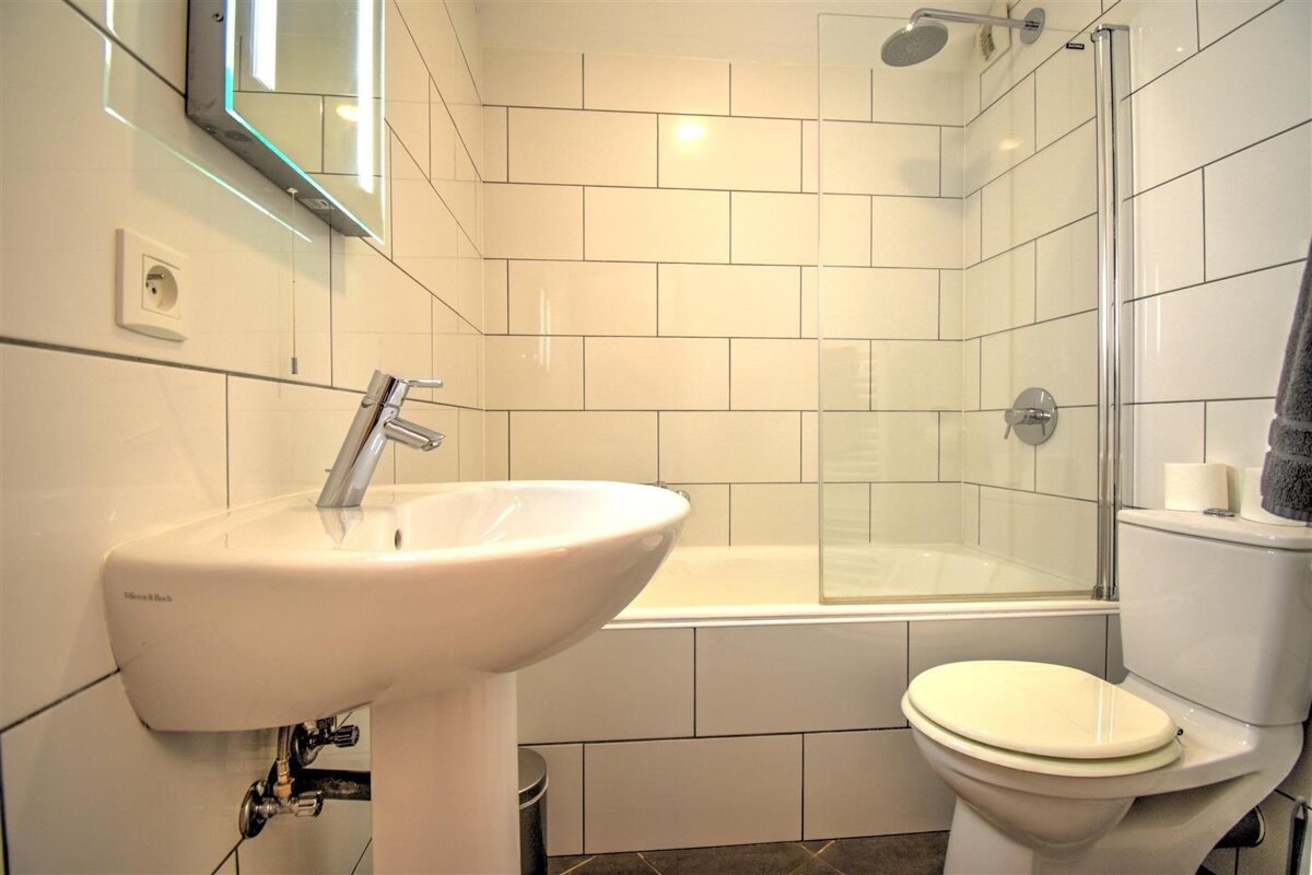 Modern bathroom with white subway tiles, featuring a pedestal sink, toilet, and a bathtub/shower combo with a glass screen.