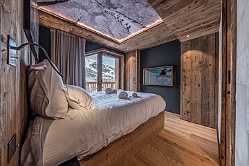 Rustic alpine chalet bedroom with wood paneling, a snowy mountain view, and a unique winter forest ceiling mural.