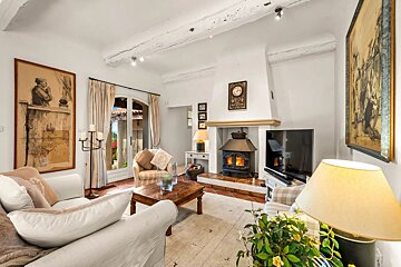 Inviting living room featuring a wood-burning stove, exposed beams, white walls, comfy sofas, and French doors to a garden.