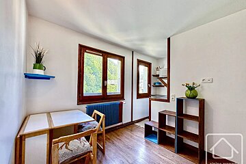 Bright, cozy room with a small dining table, wooden shelves, and windows overlooking a green landscape.