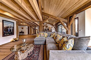 Rustic-chic living room with exposed wooden beams, a large grey sectional sofa with vibrant yellow pillows, and a unique wood and glass coffee table.