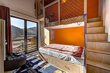 A playful room with bunk beds featuring net enclosures, an orange accent wall, space rug, wooden stairs, and a scenic mountain view.