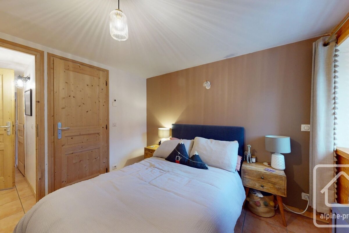An inviting bedroom features a double bed with a blue headboard, light wooden doors, and rustic nightstands. A brown accent wall complements white bedding.