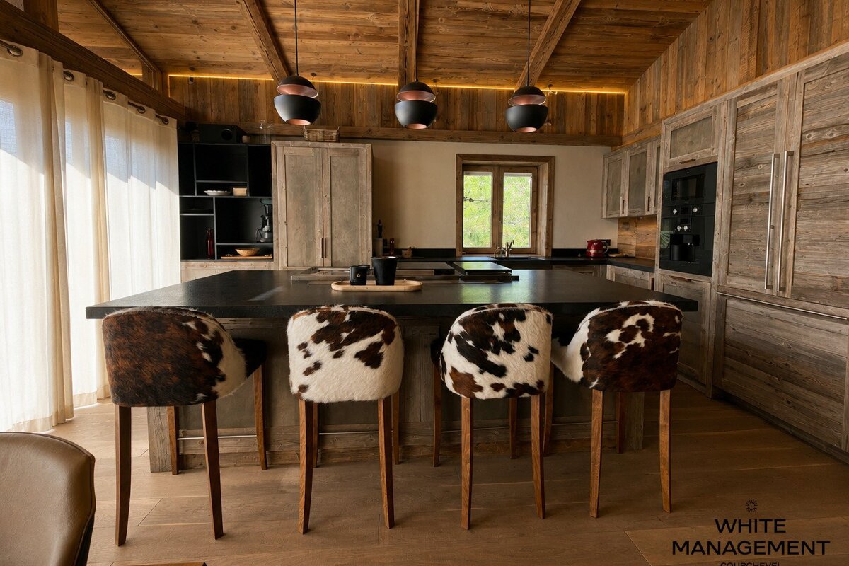 Rustic wooden kitchen featuring a black island with four cowhide bar stools and modern pendant lights.