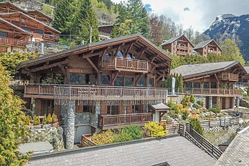 A large wooden house with a large balcony is surrounded by trees