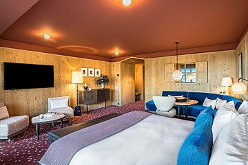 A cozy, modern room with wood-paneled walls, a red ceiling, a large bed, and a blue sofa area. Features a TV and patterned carpet.
