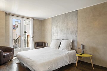 A modern bedroom featuring a bed with white bedding, textured walls, leather armchairs, and a small yellow side table.