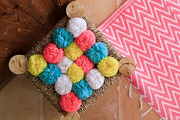 A wicker stool with colorful pom poms on it