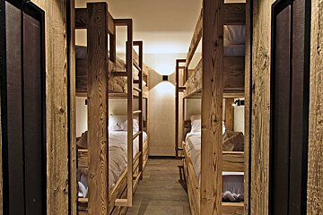 A symmetrical view of a bunk room with rustic wooden frames, white bedding, and a warm light in the distance.