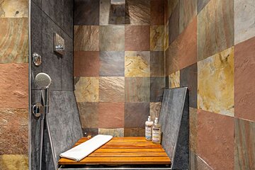 A shower with a wooden bench and two bottles of shampoo and conditioner