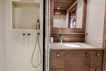 Modern bathroom featuring a beige tiled shower next to a wooden vanity with a built-in sink and matching wood-framed mirror.