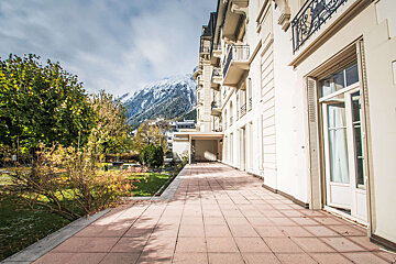 A large white building with a balcony and mountains in the background