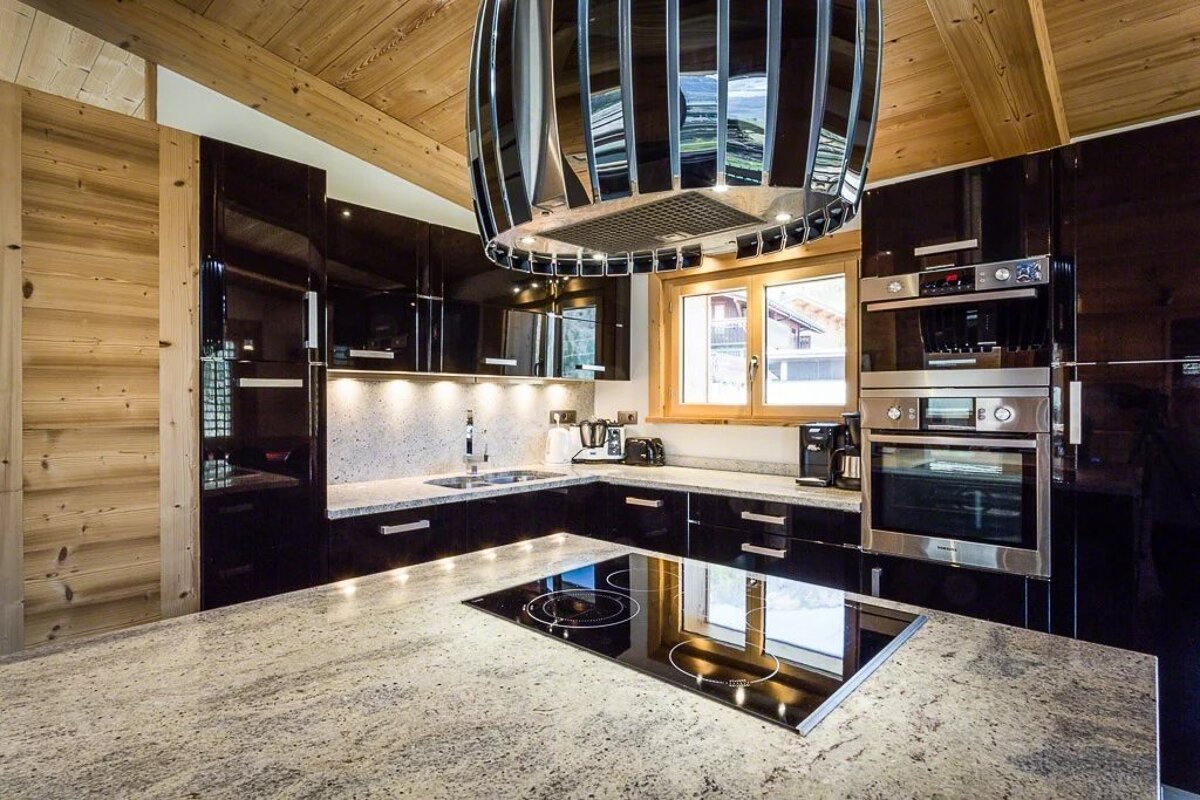 Modern kitchen in a log cabin style home, featuring glossy black cabinets, granite countertops, and a striking chrome range hood.