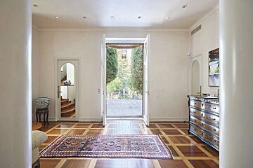 Elegant foyer with a patterned wood floor and rug. Double doors open to a beautiful garden. Features include an antique dresser and an arched doorway.