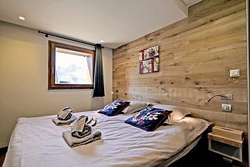 A cozy cabin bedroom with a wood-paneled accent wall, a white bed with folded towels, and a window showing snowy mountains.