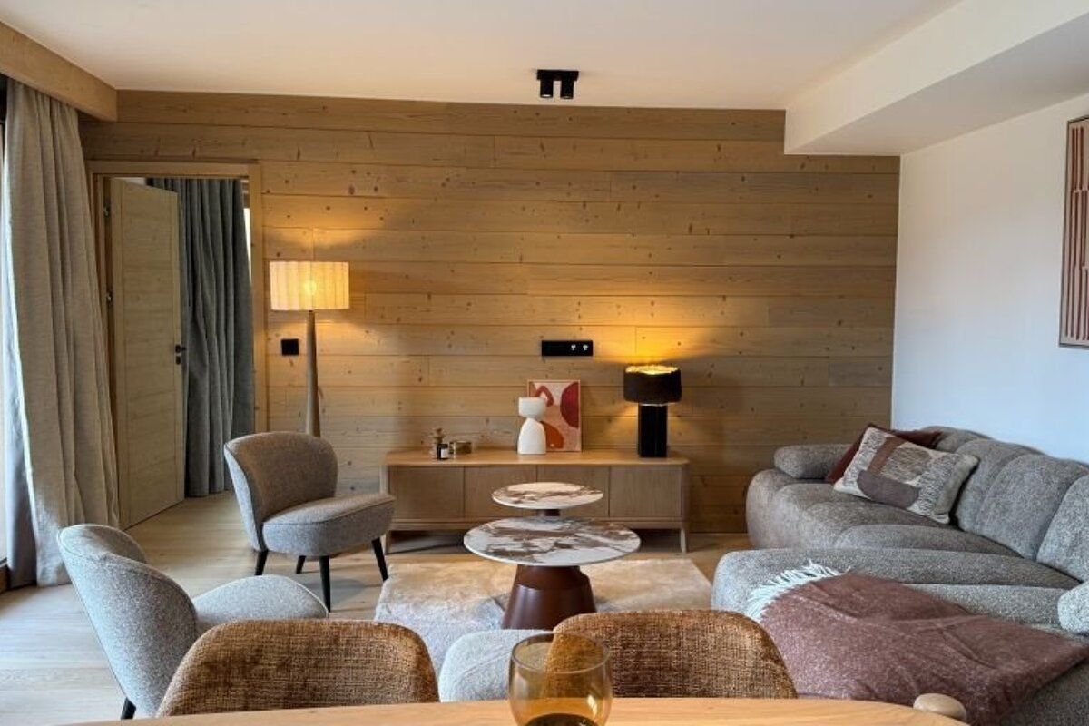 Cozy modern living room featuring a wood-paneled wall, gray seating, layered coffee tables, and warm ambient lighting.