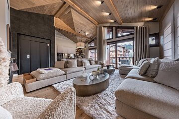Spacious, cozy modern living room with wood ceiling, plush neutral sofas, large windows revealing mountain views, and a sleek dark elevator.