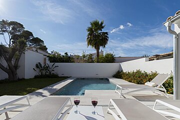 Two glasses of wine sit on a table next to a swimming pool