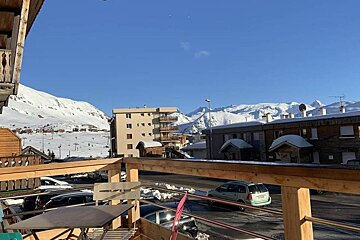 A view of snowy mountains from a balcony with a table and chairs