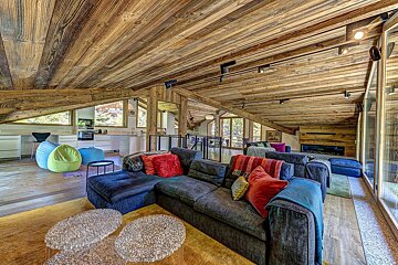 Rustic yet modern chalet interior with rich wooden ceilings, a comfy sectional sofa, and an open kitchen.