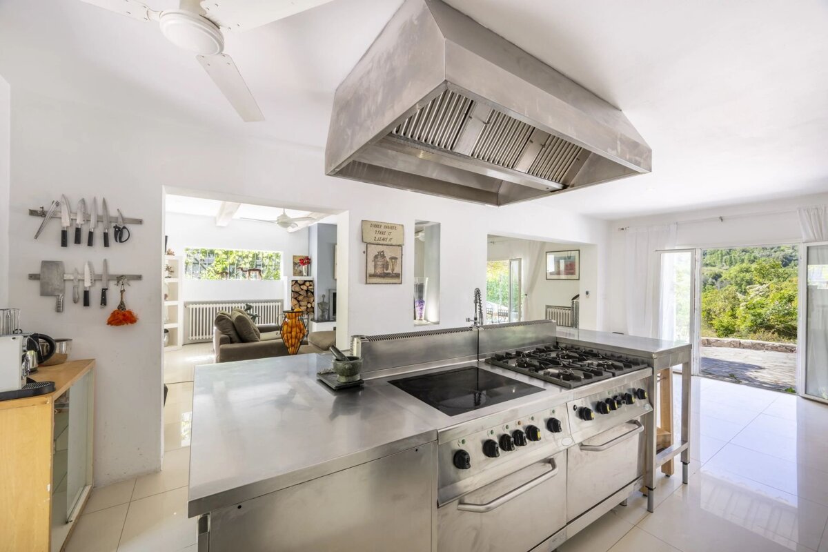 Bright, modern kitchen with a large stainless steel island, stove, and overhead range hood.