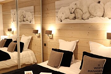 Cozy twin bedroom with wood paneling, polar bear artwork above, and a mirrored wall reflecting one bed. Warm sconces illuminate the space.