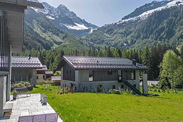 A house sits in the middle of a lush green field with mountains in the background