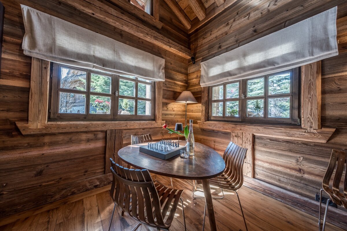 A wooden room with a table and chairs and a chess board on it