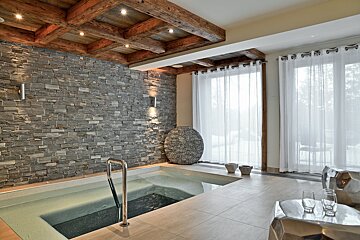 Luxurious indoor spa featuring a plunge pool, a stone accent wall, a rustic wooden ceiling, and sheer curtains.