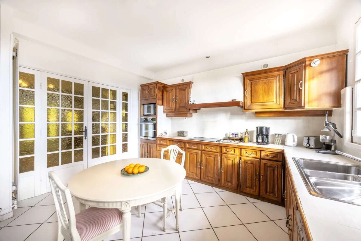 Traditional kitchen with rich wooden cabinets, white tiled floor, a round table, and glass-paned French doors.
