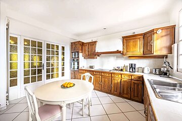 Traditional kitchen with rich wooden cabinets, white tiled floor, a round table, and glass-paned French doors.